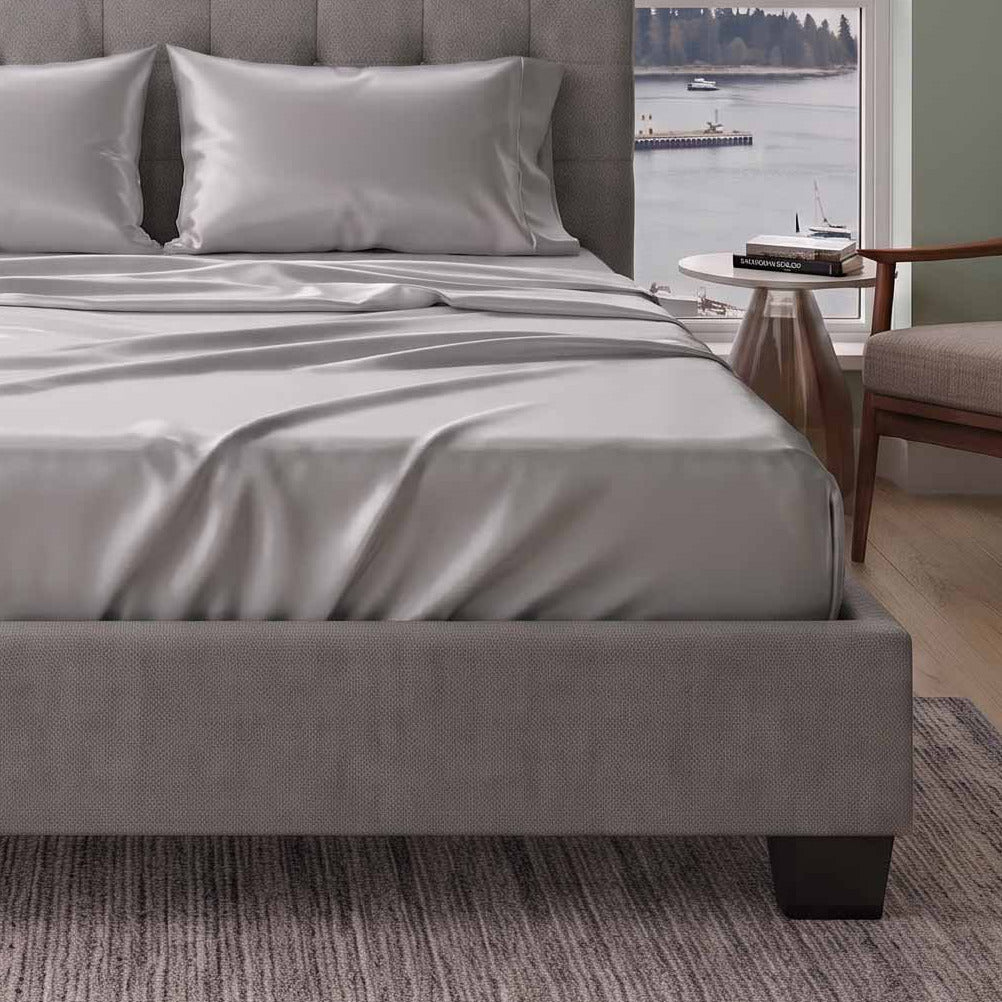A gray upholstered bed with a tufted headboard, dressed in white bedding, positioned in a modern bedroom with a large window view of mountains and the city skyline.