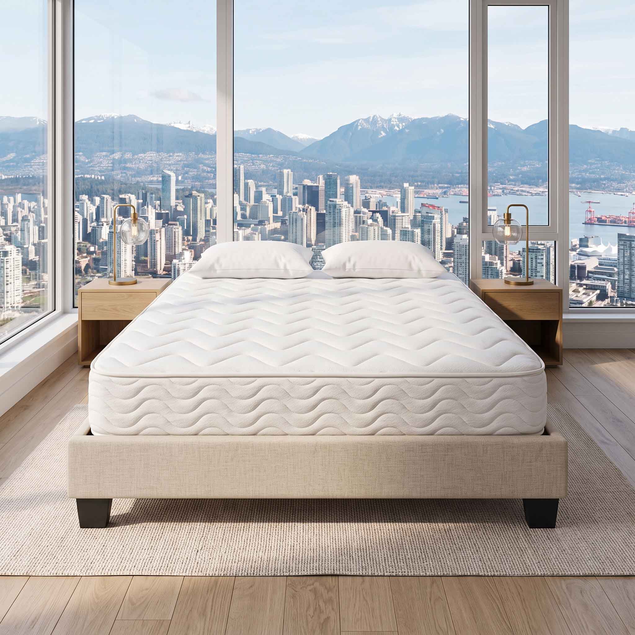 A white quilted mattress on a beige upholstered bed frame, set in a modern bedroom with a large window overlooking a city skyline and mountains.