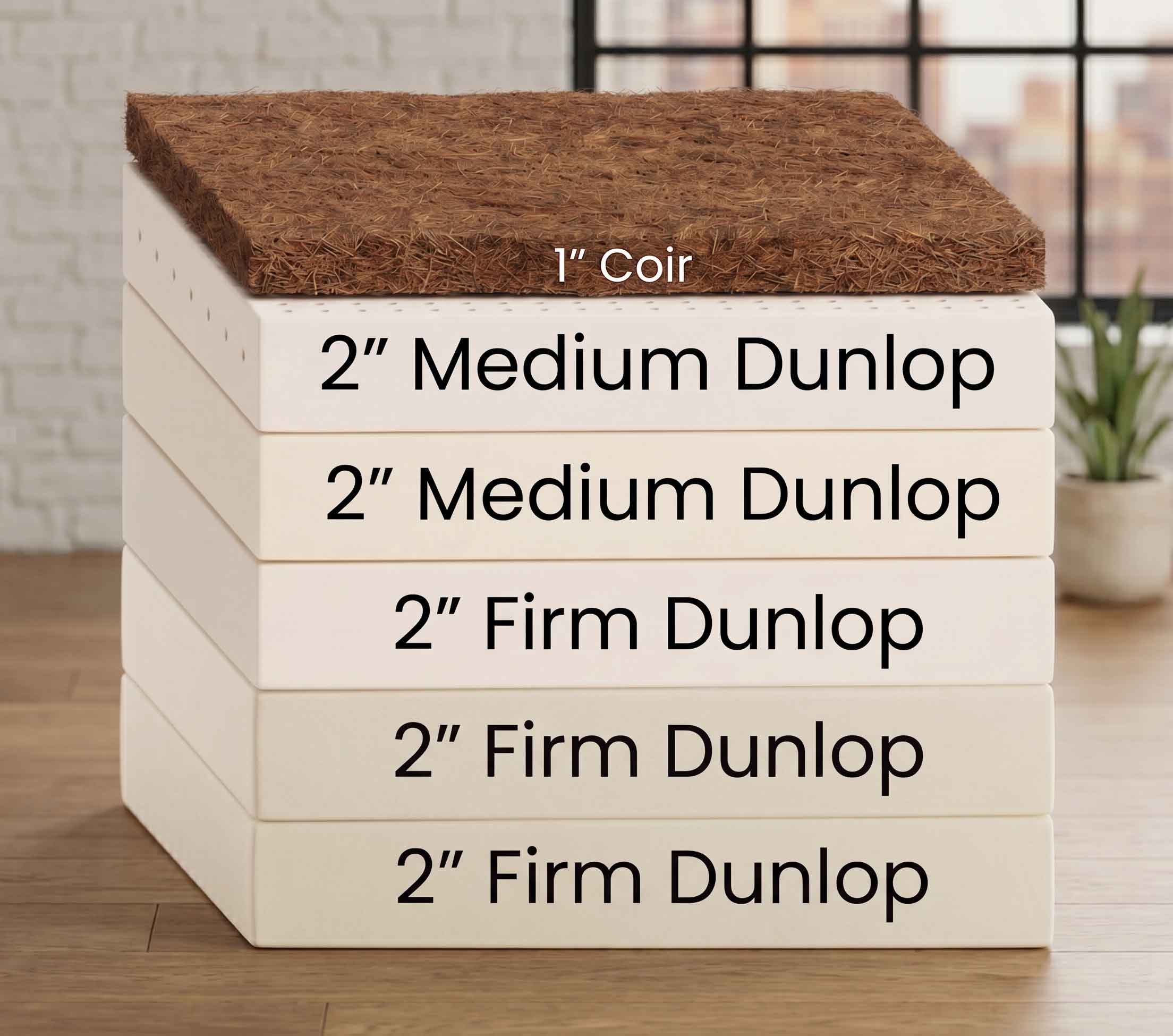 A stack of five Dunlop cotton batting panels in off-white, with a 1-inch coir top layer, shown on a wooden surface with a blurred indoor background. Text labels indicate '2" Medium Dunlop', '2" Firm Dunlop', and '1" Coir'.